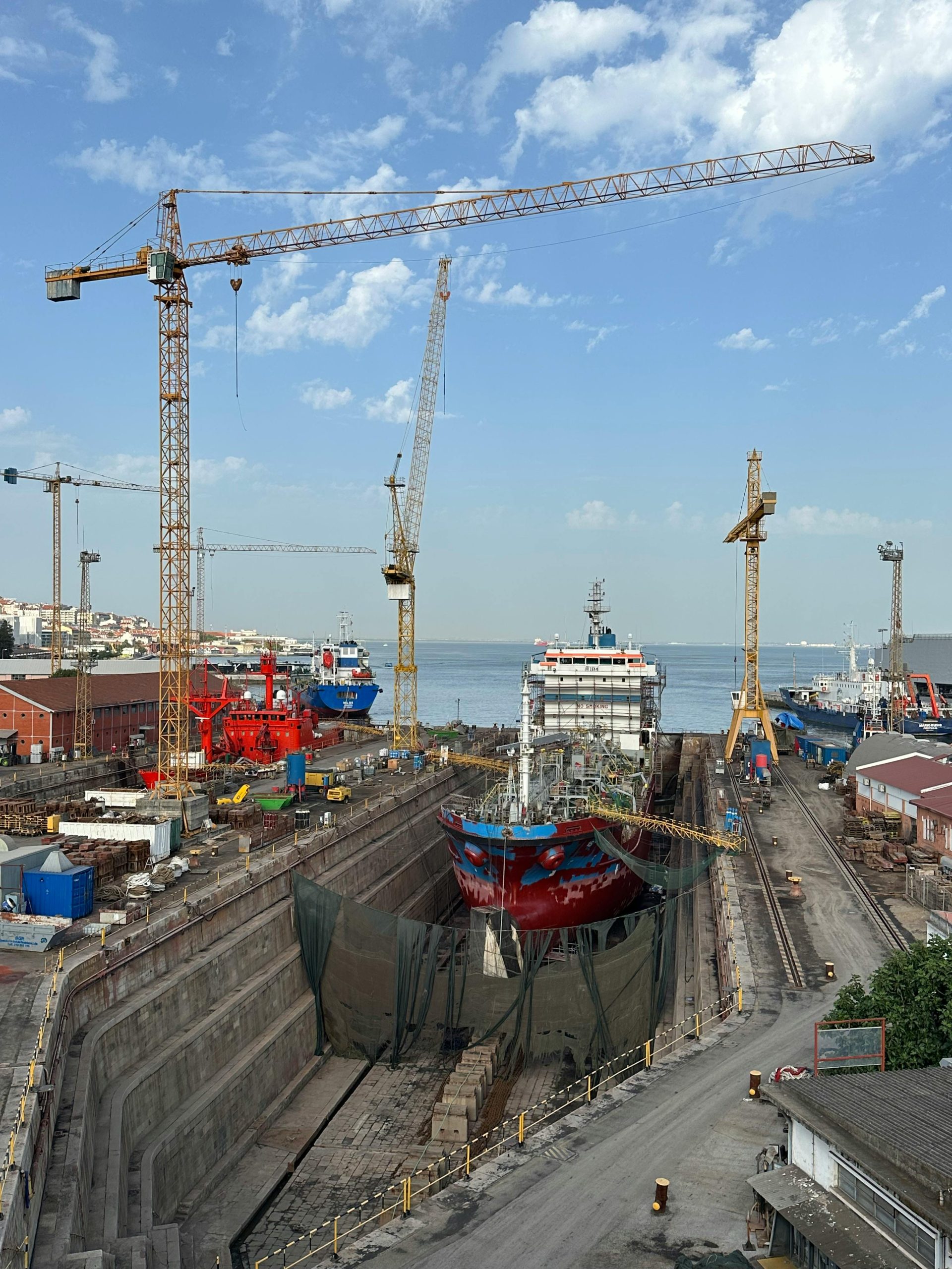 Dry Docking: Procedures and Class Society Requirements Shipyard with cranes and ships in Lisbon, Portugal harbor under blue sky.