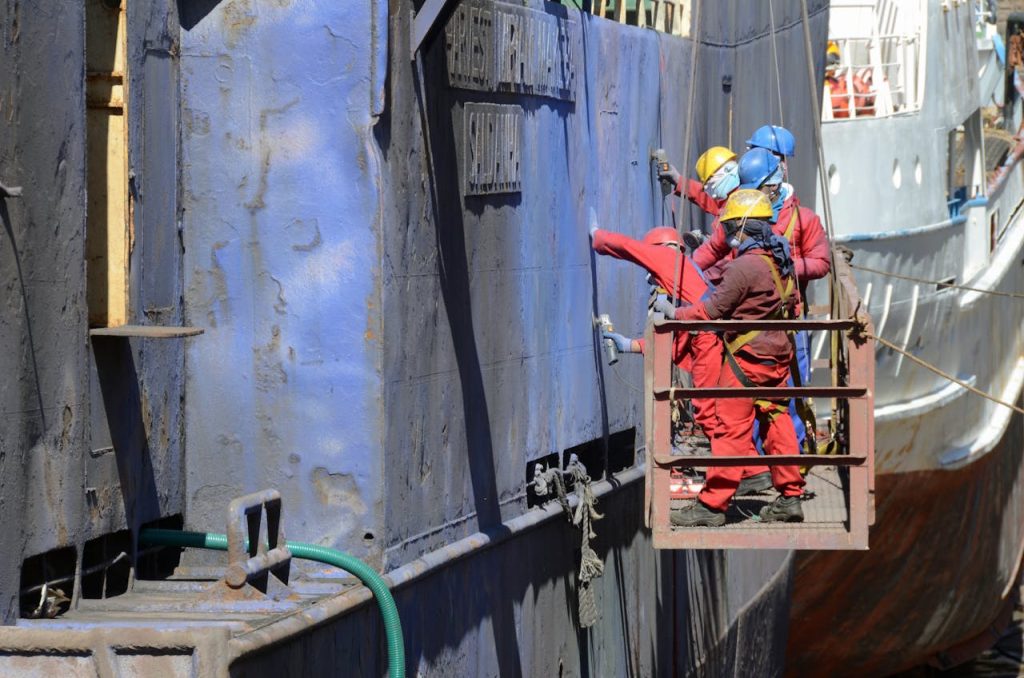 pexels photo 6638576 Workers in safety gear repairing a ship's hull at a busy shipyard.